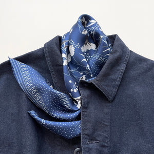 a rich blue silk scarf suits for both women and men featuring botanic leafy print and hand-rolled hems, paired with a dark blue denim top