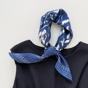 a rich blue silk scarf featuring botanic leafy and flower print and hand-rolled hems knotted as a headband, paired with a black sleeveless dress