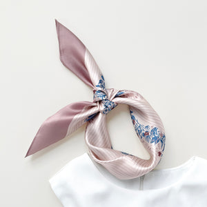 a blush pink silk scarf for women featuring blue and burgundy leafy print knotted as a neckerchief or head band, paired with a white sleeveless dress