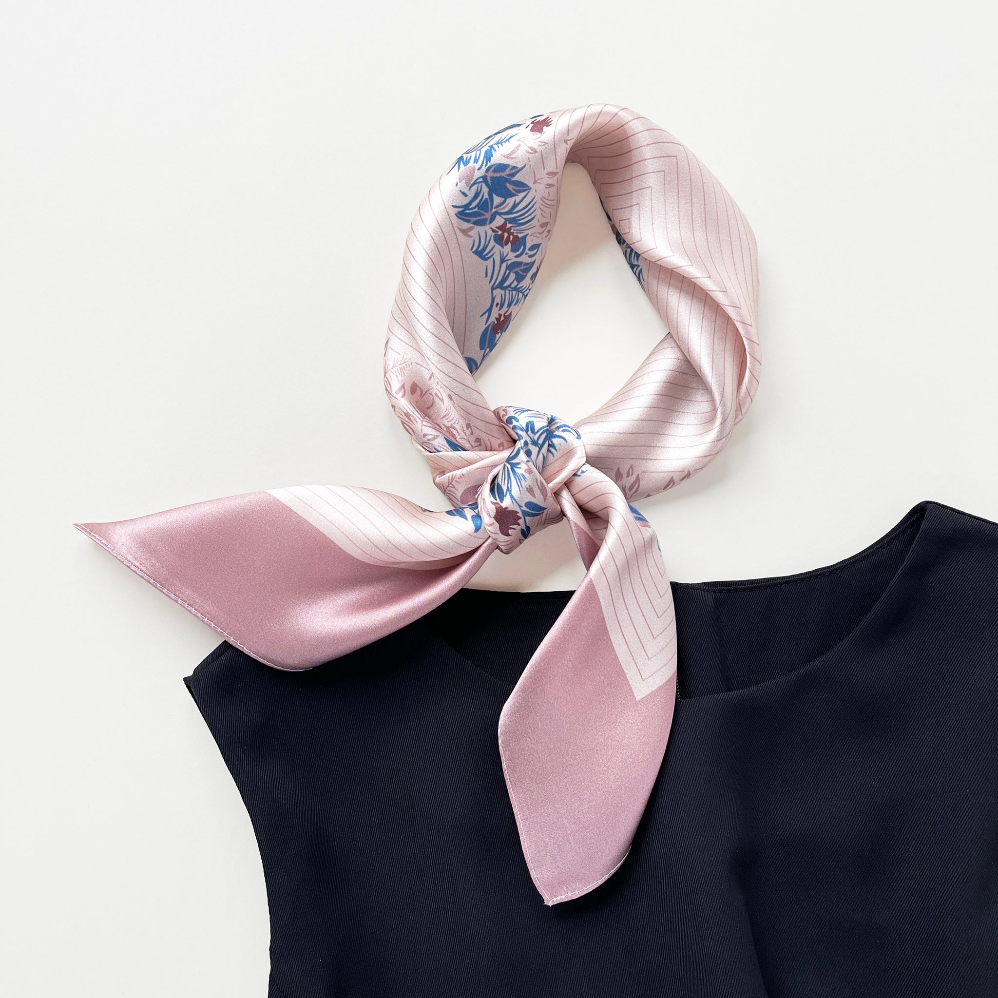 a blush pink silk scarf for women featuring blue and burgundy leafy print knotted as a neck scarf, paired with a black sleeveless dress