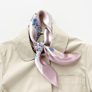 a blush pink silk scarf for women featuring blue and burgundy leafy print knotted as a neck scarf, paired with a beige coat