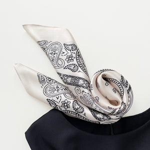 a light beige silk scarf featuring black paisley print, paired with a black sleeveless dress