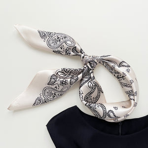 a light beige silk scarf featuring black paisley print knotted as a neck scarf or head band, paired with a black sleeveless dress