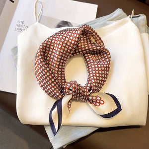a small square silk scarf with navy blue edge featuring red circle print, knotted as a neck scarf, paired with a women's white blouse and light blue jeans
