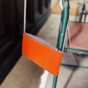 an orange small crossbody phone purse with handmade button hanging on a chair