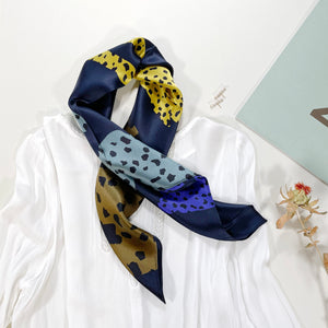 a leopard print square silk scarf in navy blue, indigo blue, yellow, black and bronze hues tied as a neck scarf paired with a women's white blouse