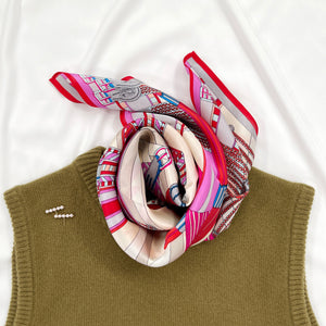 a vibrant silk scarf in magenta, red, ash grey and light beige palette tied around the neck , paired with an olive green cashmere vest 
