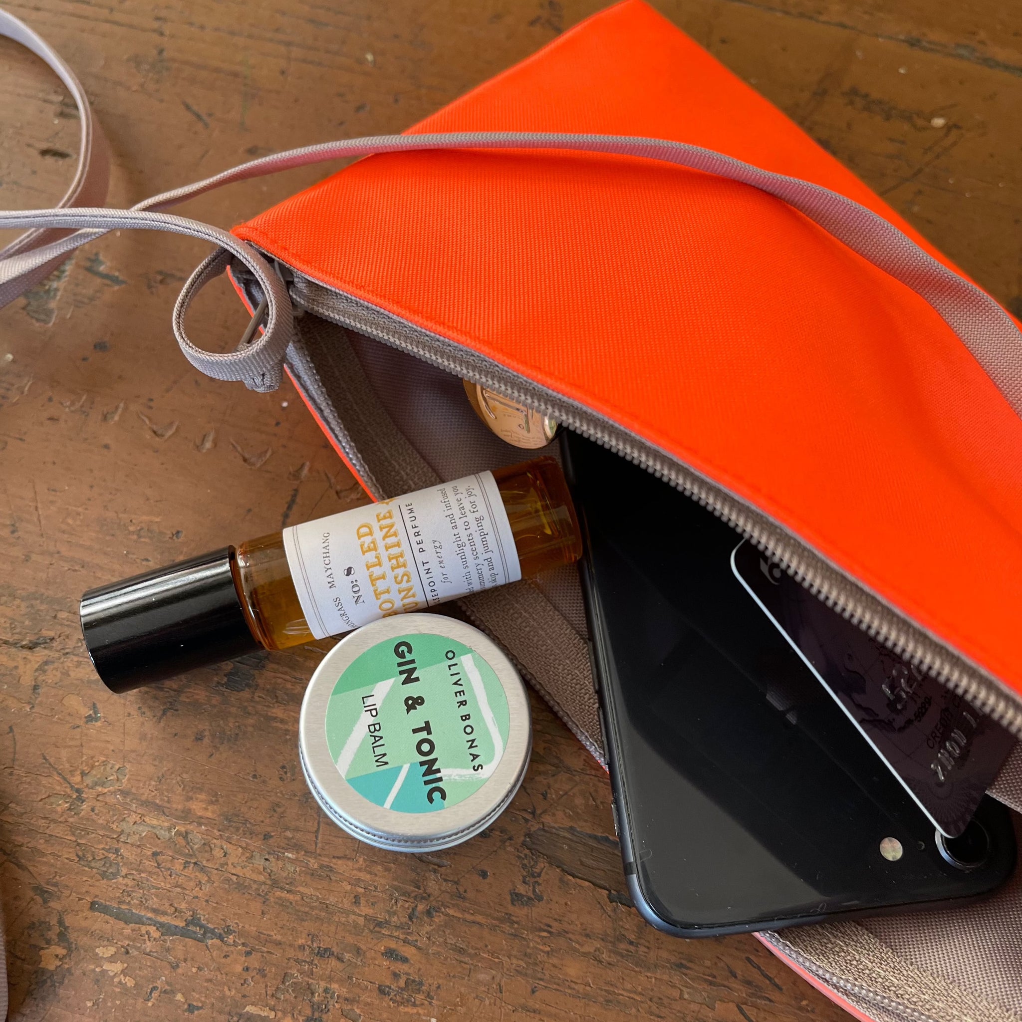 an orange fabric small crossbody phone purse with a phone, credit card, lip balm inside