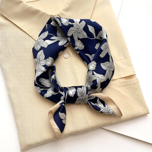 a deep blue silk bandana scarf featuring floral print with light beige edges, tied as a neck scarf, paired with a light beige turtleneck shirt