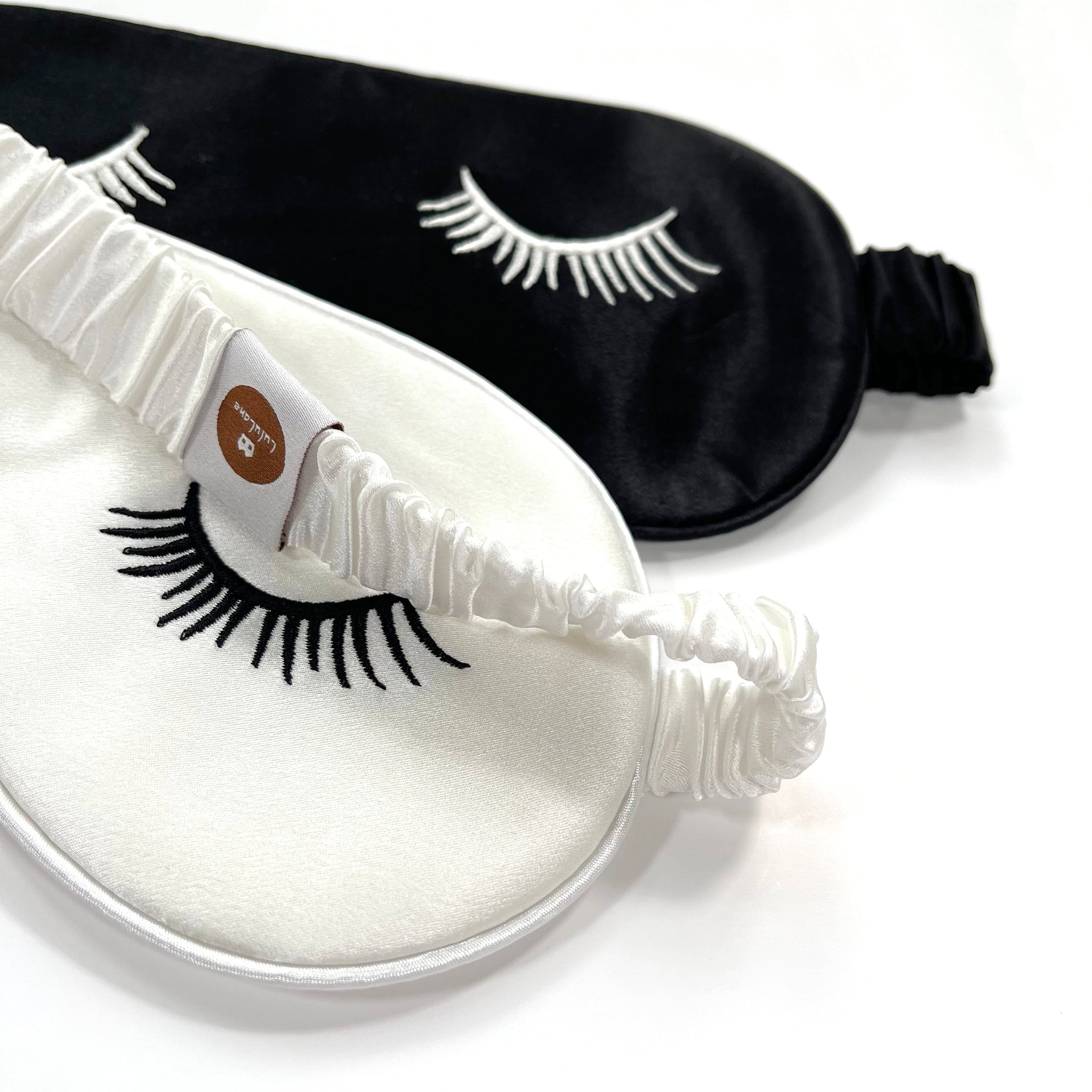two silk eye masks featuring eyelashes embroidery and elastic strap in black and white