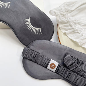 a grey silk eye mask featuring white eyelashes embroidery and elastic strap