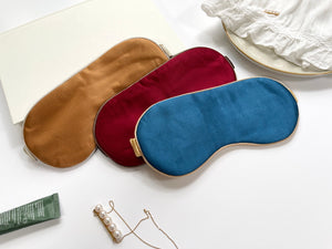 three professionally designed and handcrafted silk eye masks with elastic straps. One is burnt orange with champagne strap, one is red with brown strap, the third one is blue with light gold strap