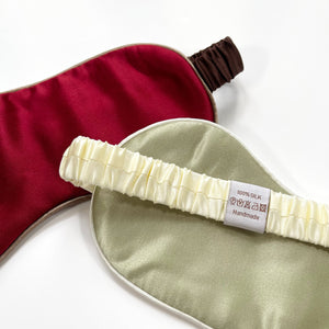 two professionally designed and handcrafted silk eye masks with elastic straps. One is red with brown strap, the other is pea green with creamy white strap