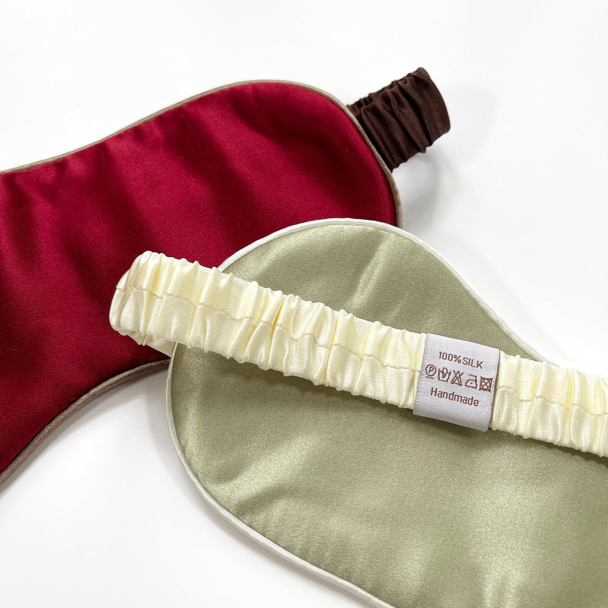 a red silk eye mask with brown strap and a pea green silk eye mask with creamy white strap